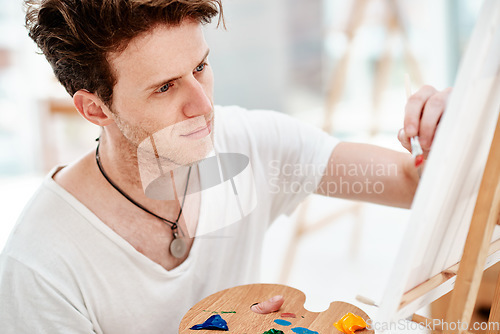 Image of Everything you can imagine is real. Cropped shot of a handsome young artist sitting alone and painting during an art class in the studio.