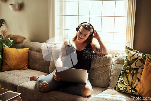 Image of Sundays are for marathon movie streaming sessions. Shot of a young woman using a laptop and headphones on the sofa at home.