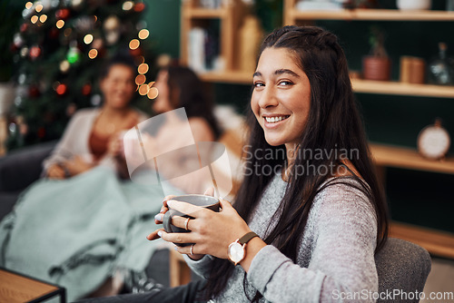 Image of Hearts come home from Christmas. Shot of a beautiful young woman enjoying a warm beverage with her friends in the background during Christmas at home.