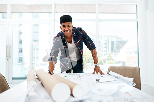 Image of At the head of the design helm. Portrait of a young man going over blueprints in a modern office.