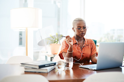 Image of A goal is a dream with a deadline. Shot of a young businesswoman wearing earphones while working on a laptop in an office.