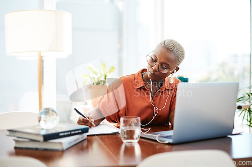 Image of Dream big and do bigger. Shot of a young businesswoman wearing earphones while writing notes in an office.