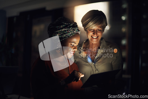 Image of Optimising their time with technology. Shot of two businesswomen using a digital tablet together in an office at night.