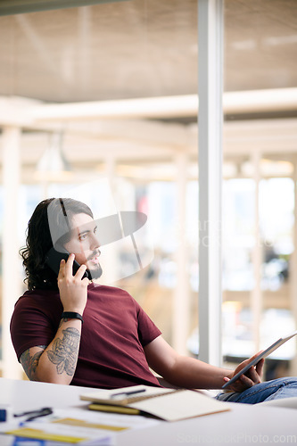 Image of Do you have any news for me. Shot of a young businessman talking on a cellphone while using a digital tablet in an office.