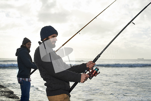 Image of Secretly hoping hell hook the bigger fish...Shot of two young men fishing at the ocean in the early morning.