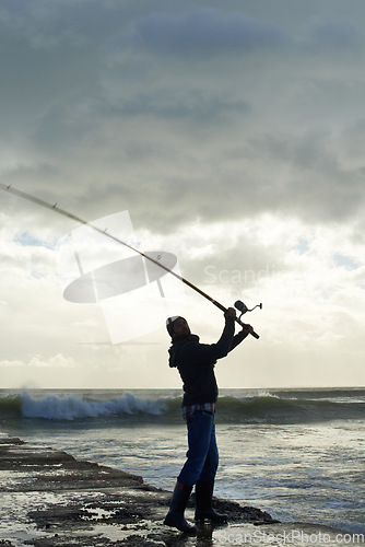 Image of Taking his time for the big catch. Shot of a solo fisherman fishing off a pier at the ocean.