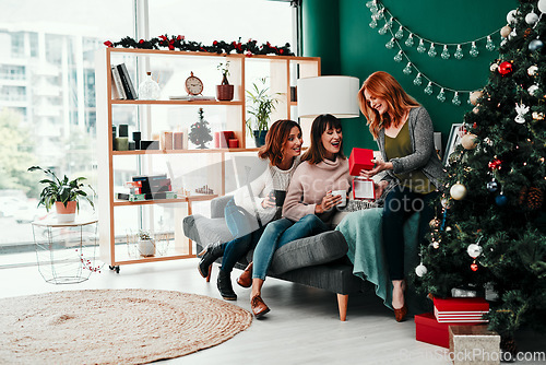 Image of This is such a nice gift. Shot of three attractive middle aged women opening presents together while being seated on a sofa during Christmas time.