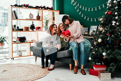 Image of Thank you both very much. Shot of three attractive middle aged women opening presents together while being seated on a sofa during Christmas time.