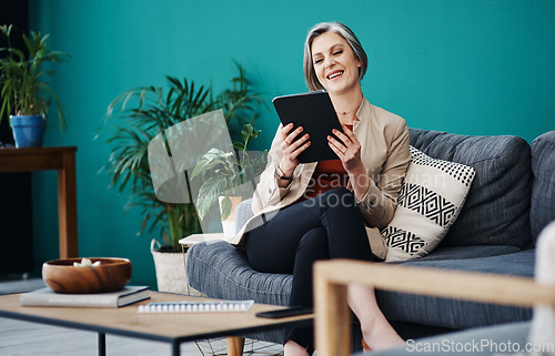 Image of The business seems to be doing well. Cropped shot of an attractive mature businesswoman sitting alone and using a tablet in her home office.