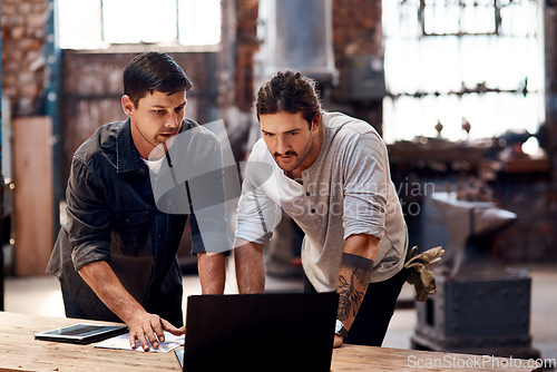 Image of Teamwork divides the work and multiplies the success. Cropped shot of two handsome young using a laptop while working together inside their workshop.