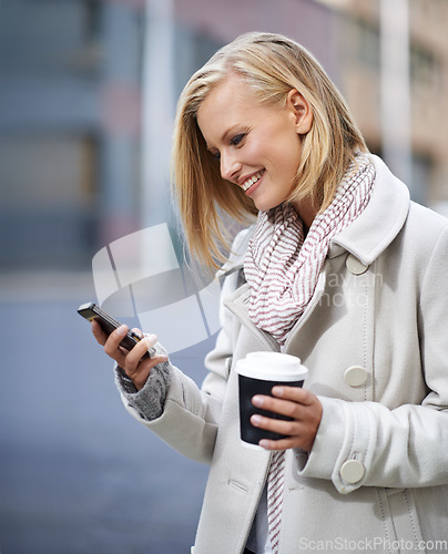 Image of On the move and always in touch. Shot of an attractive woman standing outside holding a cup and reading a text message.