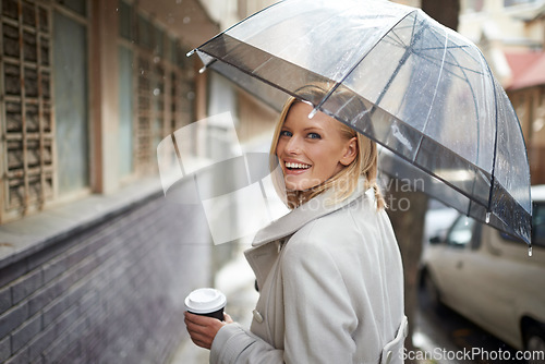 Image of Enjoying a walk in the rain. Shot of a young woman walking down the street with an umbrella on a rainy day.