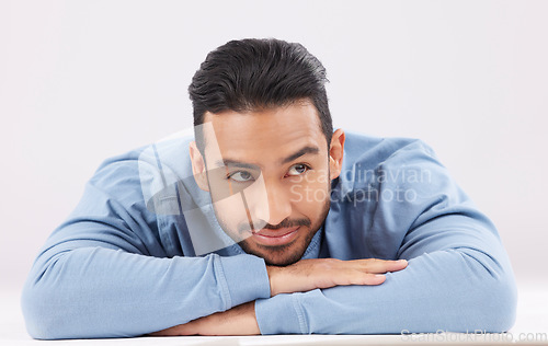 Image of Thinking, dreaming and young man in a studio resting on his arms with a contemplating facial expression. Happy, smile and Indian male model with question or remember face isolated by white background