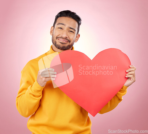 Image of Heart, happy and love with portrait of man in studio for romance, date and valentines day. Kindness, support and hope with person and sign on pink background for wellness, peace and creative mockup