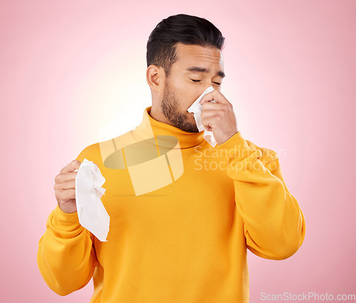 Image of Sick, tissues and man blowing his nose in a studio with a cold, flu or sinus allergies. Illness, hayfever and Indian male person with paper napkin for virus or infection symptoms by a pink background