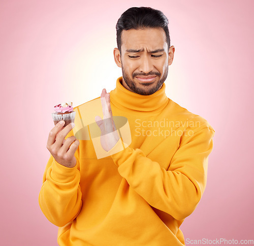 Image of Man, cupcake and studio for diet choice, thinking or bad review for gluten allergy, health or pink background. Gen z guy, student or fashion model with muffin, cake or decision for nutrition feedback