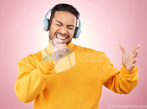 Image of Asian man, headphones and listening to music while singing for karaoke against a pink studio background. Happy male person enjoying online audio streaming, sound track or songs with headset on mockup