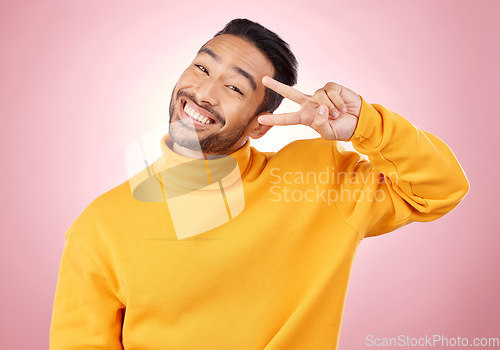 Image of Smile, peace sign and portrait of man in studio for support, kindness and happy. Emoji, happiness and thank you with face of person on pink background for mindfulness, vote and v hand gesture