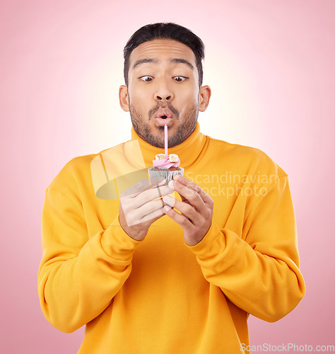 Image of Food, cupcake and man blowing candle in studio for celebration, party and dessert. Birthday, wish and flame with face of male person and cake on pink background for surprise, candy and gift mockup