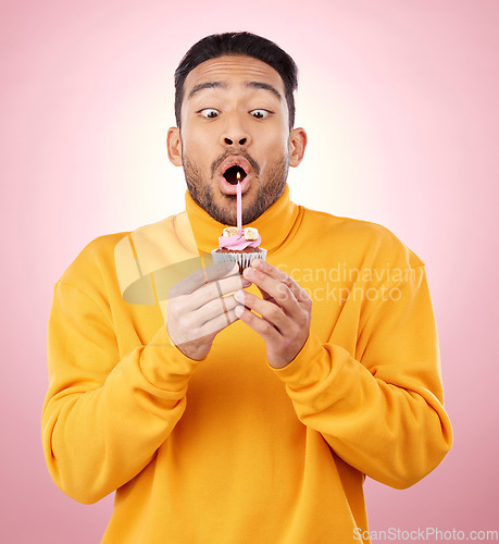 Image of Birthday, cupcake and man blowing candle in studio for celebration, party and dessert. Food, wish and flame with face of male person and cake on pink background for surprise, candy and gift mockup