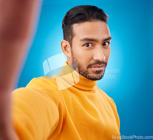Image of Selfie, face and portrait of a young man in studio with hand, style and fashion clothes. Serious male asian model on a blue background for social media, platform or network profile picture update