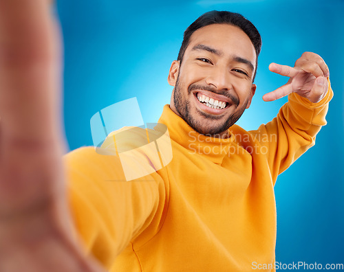 Image of Selfie, happy and peace sign portrait of a man in studio with hand, emoji and a smile. Male asian fashion model on a blue background with a positive mindset for social media profile picture update