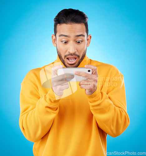 Image of Phone, reading and a shocked man in studio with a secret, gossip or fake news on social media. Male asian model watch video or post on smartphone for wow, surprise or chat on a blue background