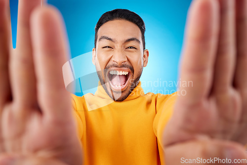 Image of Selfie, excited and portrait of a man in studio with hands and shout emoji. Face of asian male or fashion model on blue background with surprise and fun energy for social media profile picture update