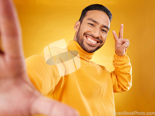 Image of Selfie, peace sign and happy portrait of a man in studio with hand, emoji and a smile. Male asian fashion model on a yellow background with a positive mindset for social media profile picture update