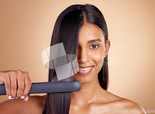 Image of Portrait, hair and flat iron with a woman in studio on a beige background for beauty or style. Face, smile and haircare with happy young female model using a straightener appliance for natural care