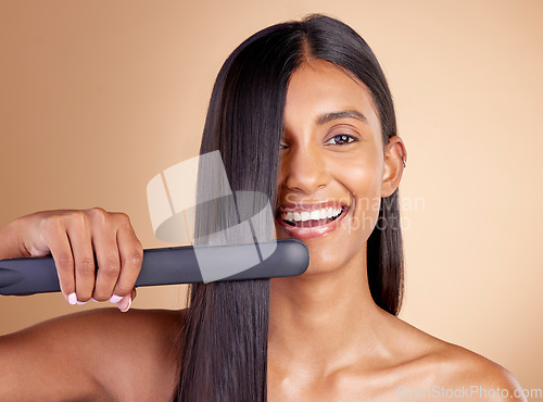 Image of Portrait, hair and flat iron with a model woman in studio on a beige background for beauty or style. Face, smile and haircare with happy young female using a straightener appliance for natural care