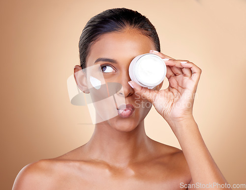 Image of Woman, cream container thinking of eye skincare, dermatology health and cosmetics. Facial product, kiss face and young person or beauty model with skin care lotion on a studio, brown background