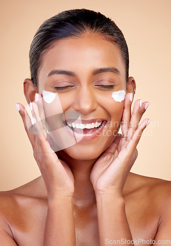 Image of Cream, face and happy woman for beauty cosmetics, dermatology or aesthetic makeup on studio background. Indian female model, lotion and smile with facial sunscreen for clean skincare, glow and shine