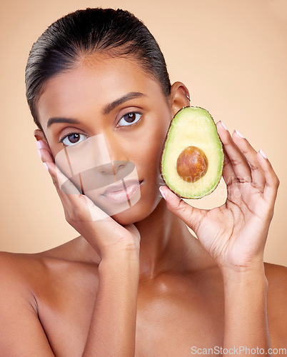 Image of Avocado, beauty and woman in portrait for healthy face and natural skincare on studio brown background. Young indian person or model with green fruits, vitamin c benefits and dermatology or cosmetics