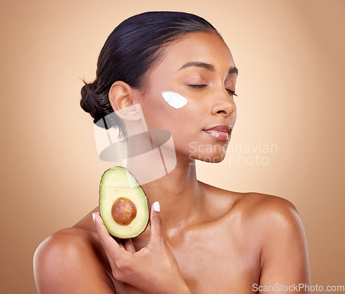 Image of Woman, avocado and cream for skincare, natural beauty and vitamin c benefits on studio, brown background. Young calm person or model with facial, green fruits and skin care moisturizer in dermatology