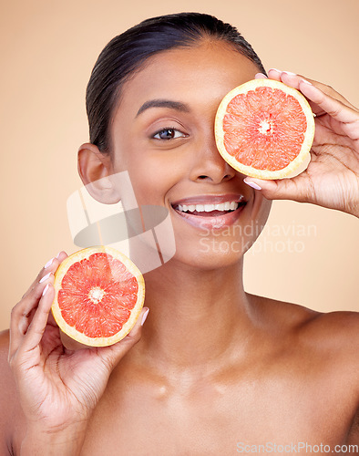 Image of Skincare, woman and grapefruit on eye for beauty, cosmetics and natural product, health or vitamin c in portrait. Face of indian person or model, red fruit and dermatology on studio, brown background