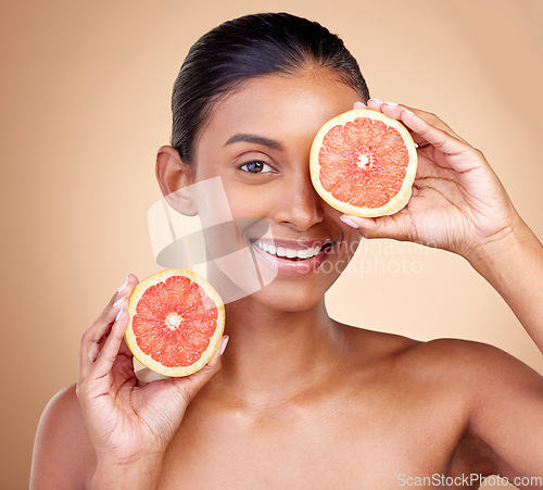 Image of Beauty, woman and grapefruit on eye for skincare, cosmetics and natural product, health or vitamin c in portrait. Face of indian person or model, red fruit and dermatology on studio, brown background