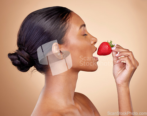 Image of Beauty, strawberry and health of a woman in studio for wellness, cosmetics and dermatology. Fruit, diet and face of a young indian person on a brown background with natural makeup, glow and shine