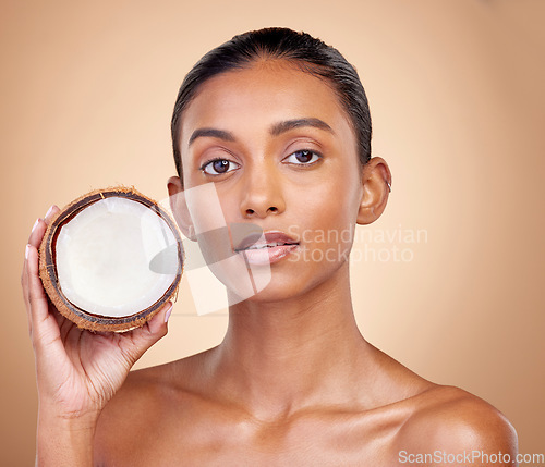 Image of Woman face, coconut fruit and beauty, healthy skincare or vegan cream on brown studio background. Portrait of Indian person in natural product for dermatology, eco friendly cosmetics and oil benefits