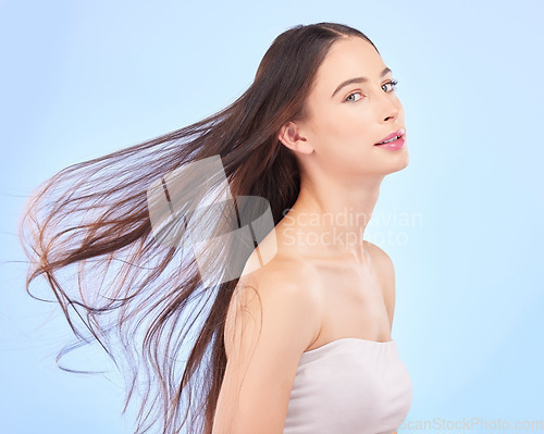 Image of Portrait, hair and wind with a model woman in studio on a blue background for skincare or keratin treatment. Spa, salon and haircare with a young female person posing for beauty or shampoo promotion