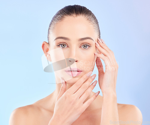 Image of Portrait, woman and touch face in studio for beauty, aesthetic glow and dermatology on blue background. Young female model feeling soft skincare, healthy cosmetics and shine of natural facial results