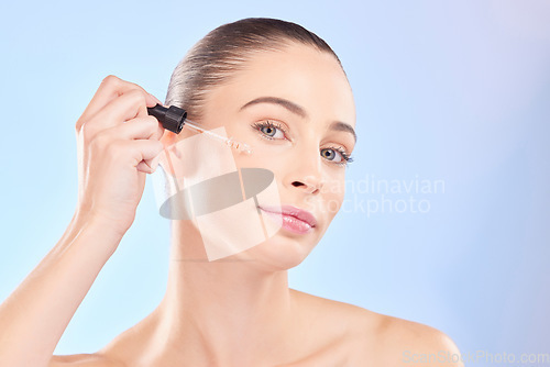 Image of Woman, portrait and oil serum for face, aesthetic skincare and dermatology on blue background. Female model, facial cosmetics and dropper of hyaluronic acid, liquid collagen and beauty glow in studio