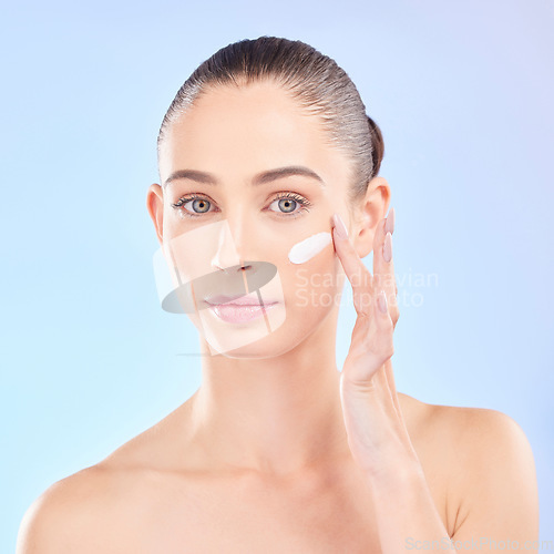 Image of Face, skincare and woman with cream in studio isolated on a blue background. Portrait, dermatology and serious model with creme, cosmetic or sunscreen moisturizer for health, aesthetic or wellness