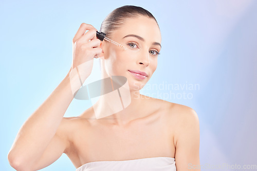 Image of Woman, portrait and serum for face in studio, aesthetic skincare or dermatology on blue background. Female model, facial cosmetics and dropper of hyaluronic acid, collagen and oil product for beauty