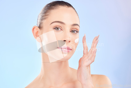 Image of Face, skincare and woman with sunscreen in studio isolated on a blue background. Portrait, dermatology and serious model with cream, beauty cosmetic or moisturizer for health, aesthetic or wellness