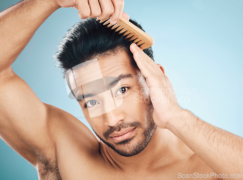 Image of Portrait, beauty and a man brushing his hair on a blue background in studio for self grooming. Face, morning and routine with a young male model in the bathroom for style after shampoo treatment