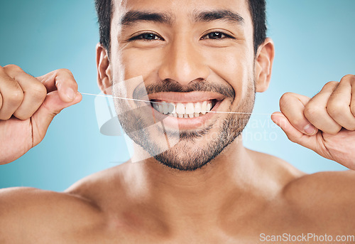 Image of Wellness, teeth and flossing of a man portrait with cleaning and dental health in a studio. Face, blue background and healthy male person with dental floss for mouth hygiene and healthcare with smile