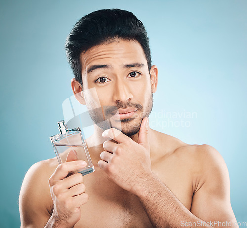 Image of Portrait, cosmetics and man with cologne, beauty or self care against a blue studio background. Face, male person or model with wellness, luxury or perfume with skincare, fragrance bottle or grooming