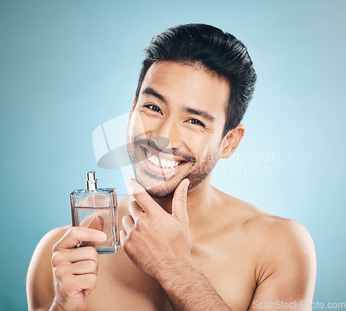 Image of Portrait, perfume and man with cologne, self care and grooming against a blue studio background. Face, male person and model with wellness, luxury and aesthetic with skincare and fragrance bottle