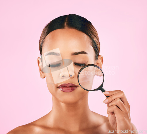 Image of Woman, face and magnifying glass, beauty and zoom in on pores, skincare and makeup isolated on pink background. Search, investigate and check skin with glow, female model and dermatology in studio